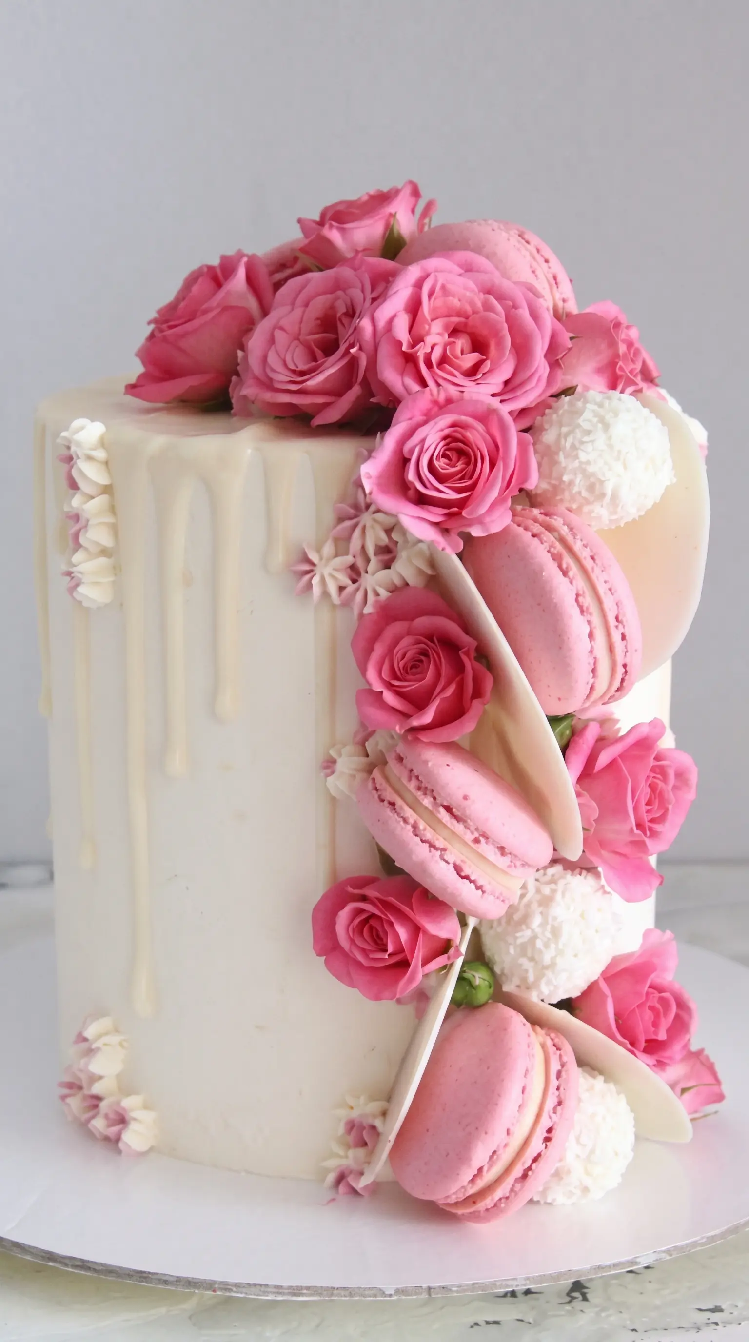 Elegant bespoke cake decorated with pink roses, macarons and white chocolate details